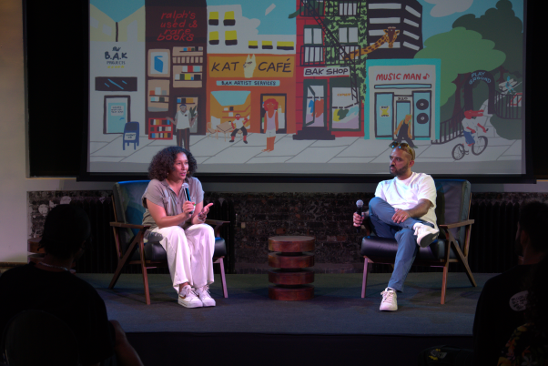 Carolyn Ortiz in a fireside chat on stage in front of an illustrated B.A.K. street-scene backdrop