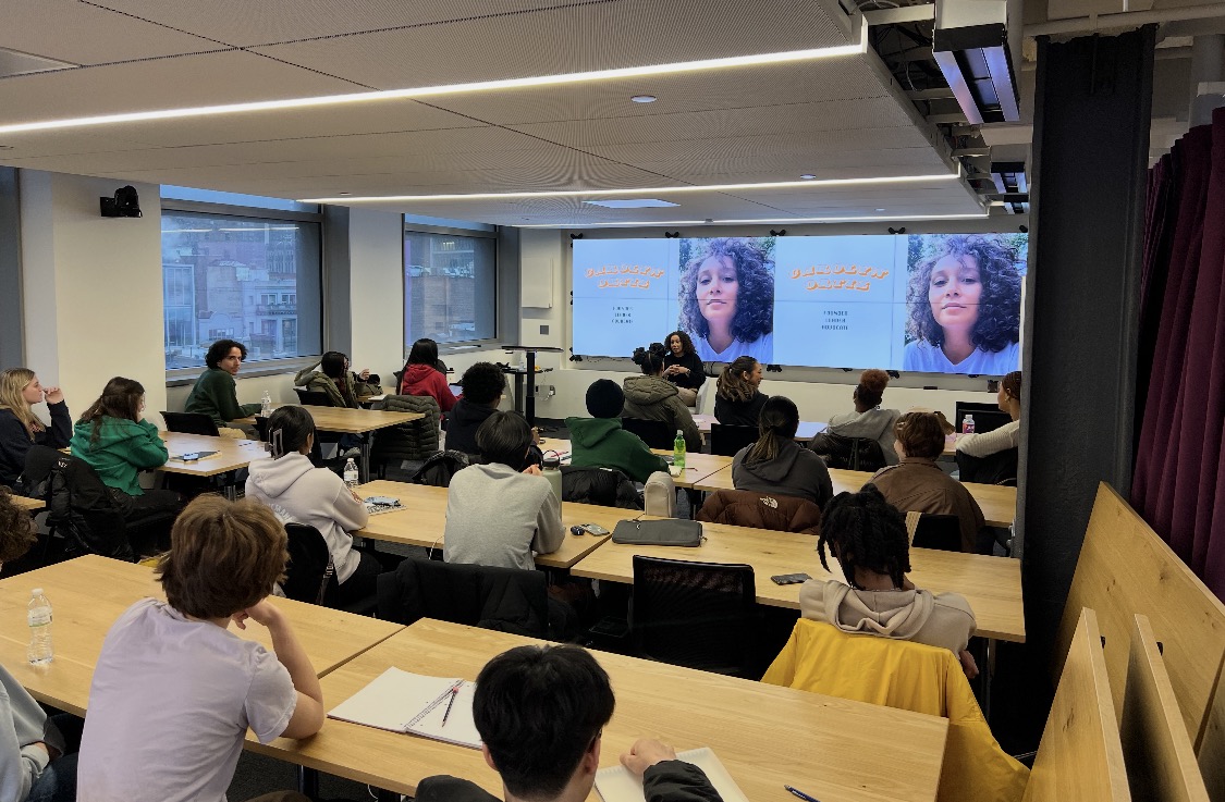 Carolyn Ortiz leading a guest lecture to a packed university classroom, her presentation projected on screens behind her