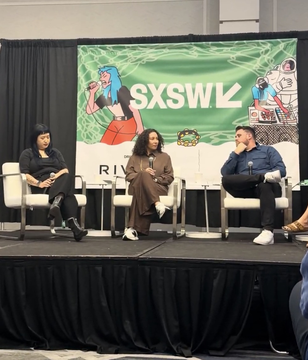 Carolyn Ortiz speaking on a panel at SXSW, seated center with a microphone in front of the SXSW banner